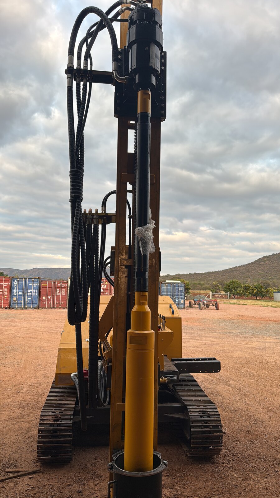 Finished JCS500 outdoors with mast raised vertical and red feed cylinder, standing on red-earth yard