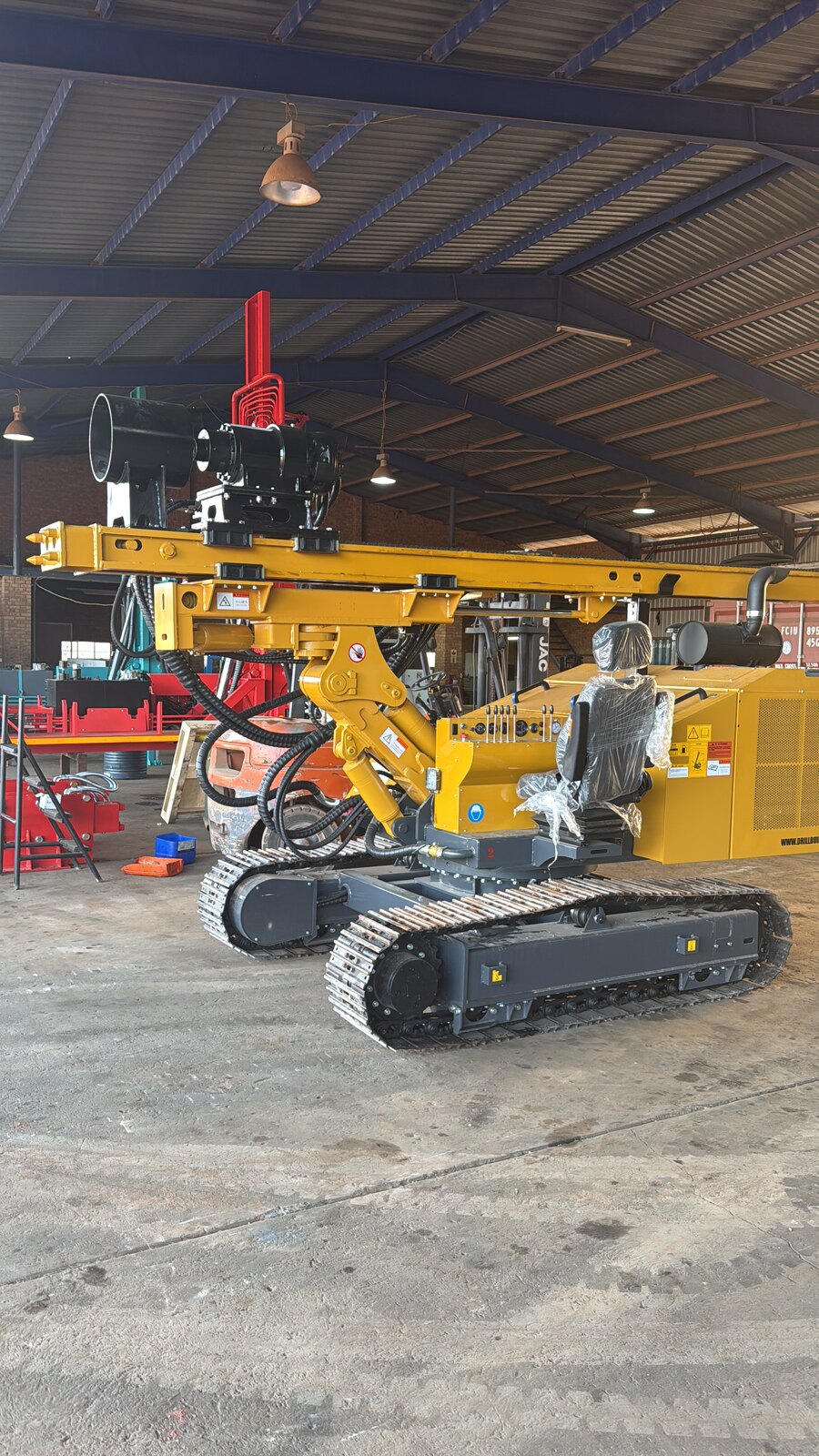 Several yellow JCS500 solar piling rigs lined up under the Drillbuilders workshop roof