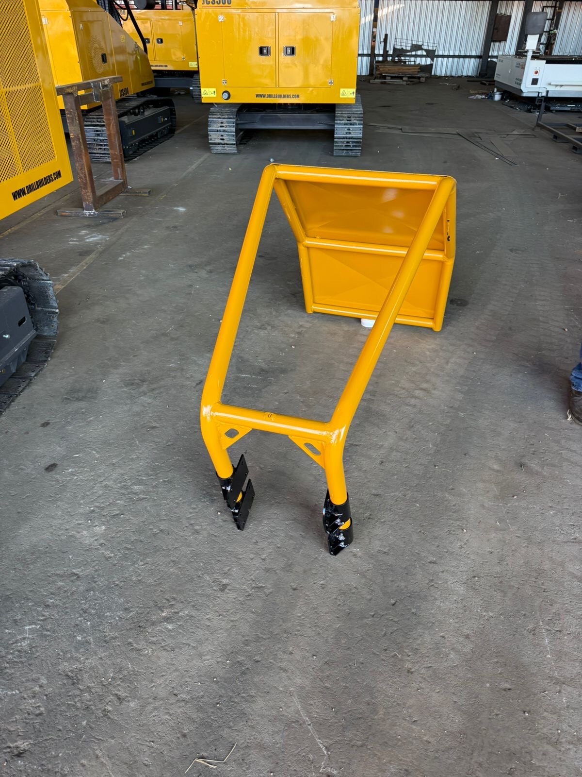 Fabricated yellow sun-canopy with a tubular roof frame on bolt-on feet, standing in the Drillbuilders workshop