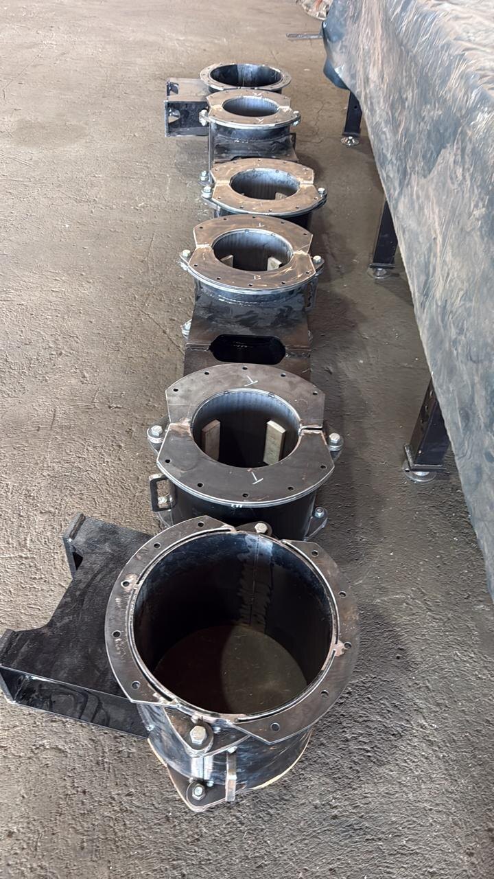 A row of six finished drill-bush guides lined up on the Drillbuilders workshop floor, each with a flanged split top, hinge and base-plate brackets