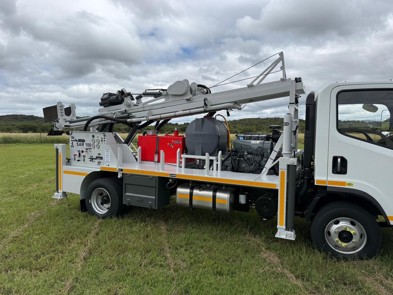 White SAR100 truck-mounted water well drilling rig with the mast stowed for travel, parked on grass in the South African bushveld