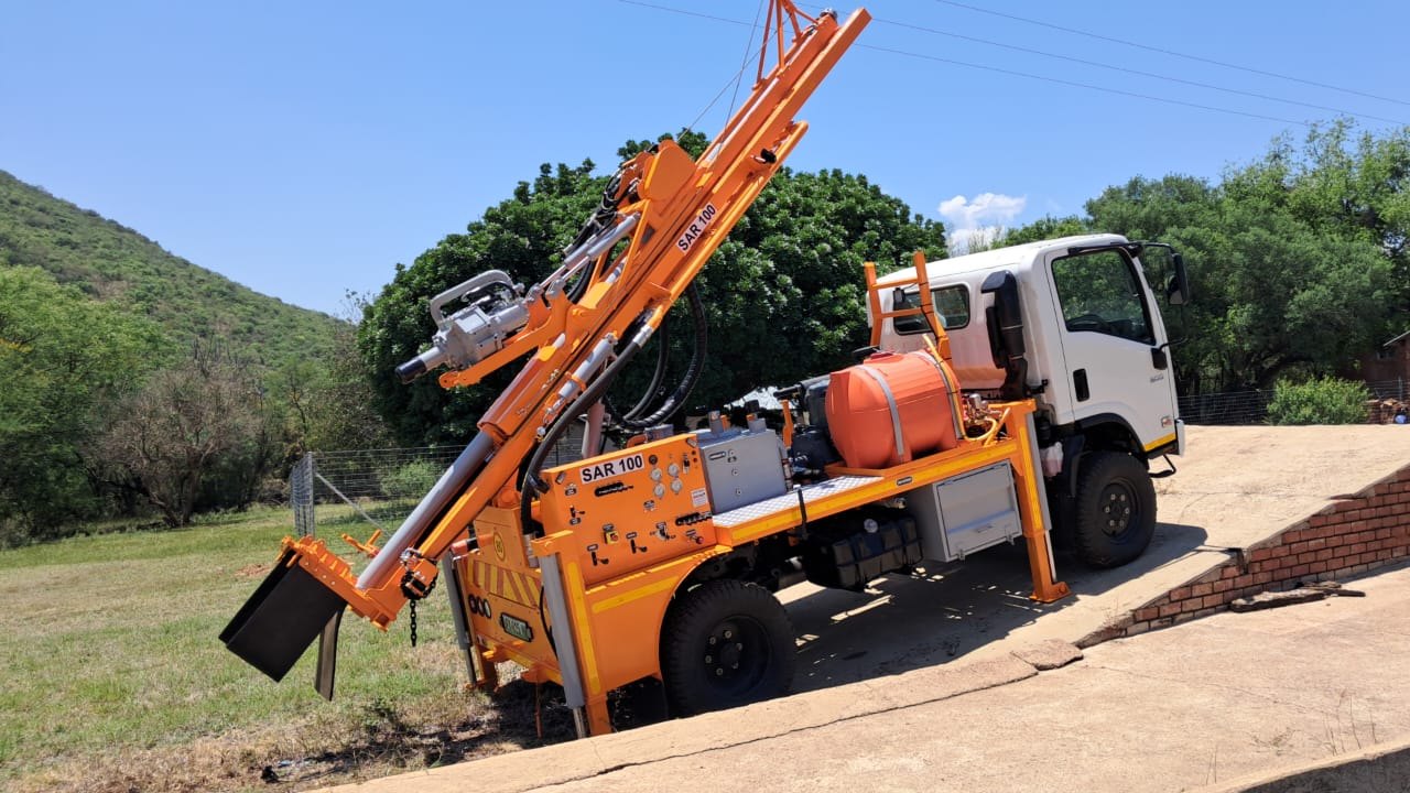 Orange SAR100 borehole drilling rig on a compact truck parked on a steep concrete ramp, showing the kind of awkward access it is built for