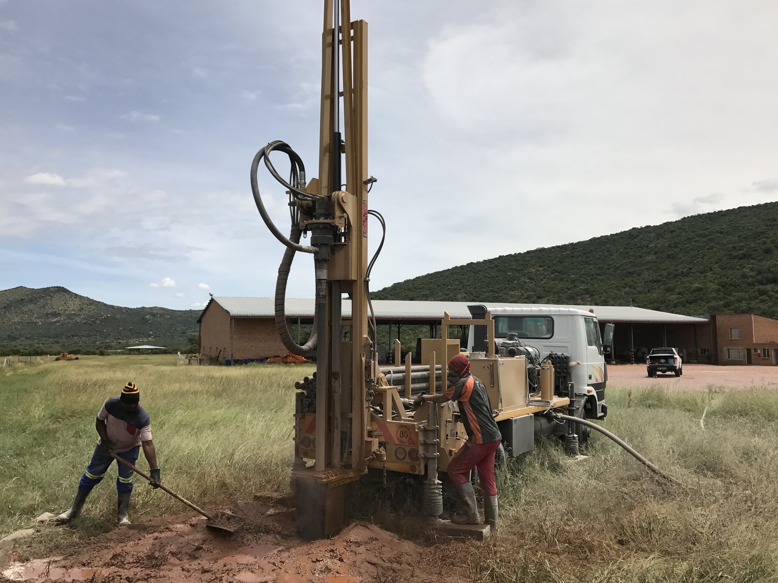 Drilling crew at work on a truck-mounted Drillbuilders rig, clearing cuttings from the borehole as the mast stands tall