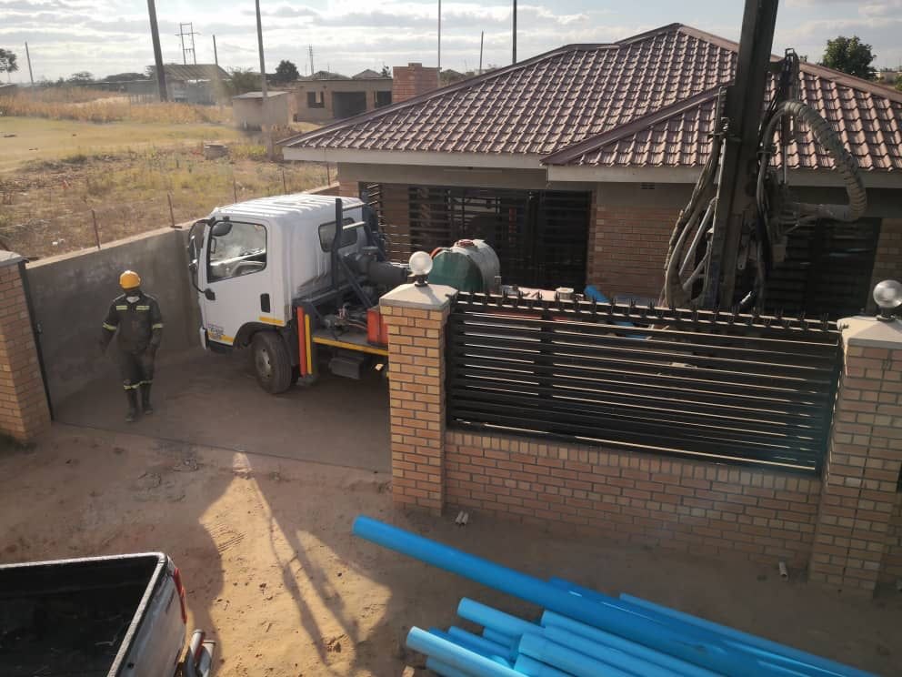 Compact truck-mounted drilling rig working inside the walled yard of a suburban house — the tight-access borehole site the SAR100 is designed for