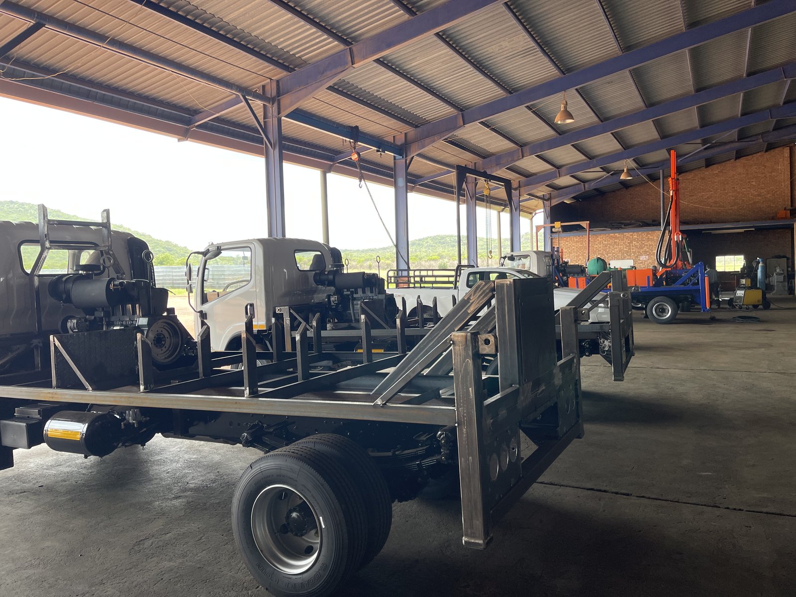 Bare-steel loadbody frame and mast supports welded onto a compact truck chassis inside the Drillbuilders workshop