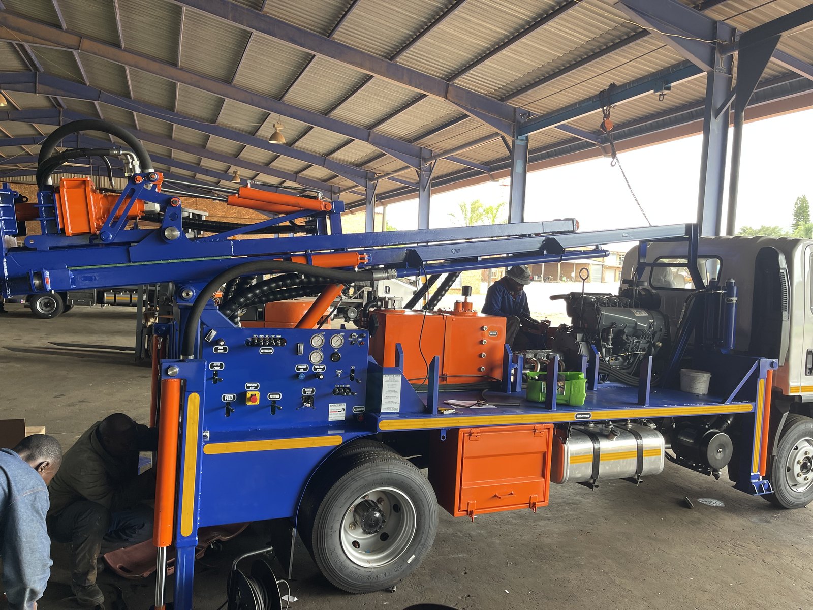 Technicians fitting the Deutz engine and hydraulics to a blue-and-orange SAR100 during final assembly