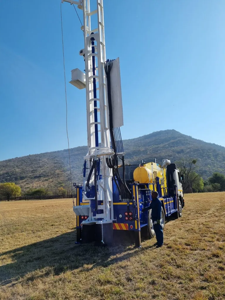 A200 drill rig with the tower raised and an operator at the controls, drilling in an open field