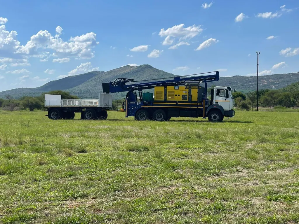 SAR200 drill rig with on-board compressor on a 6x4 truck, towing its drawbar rod trailer across a field